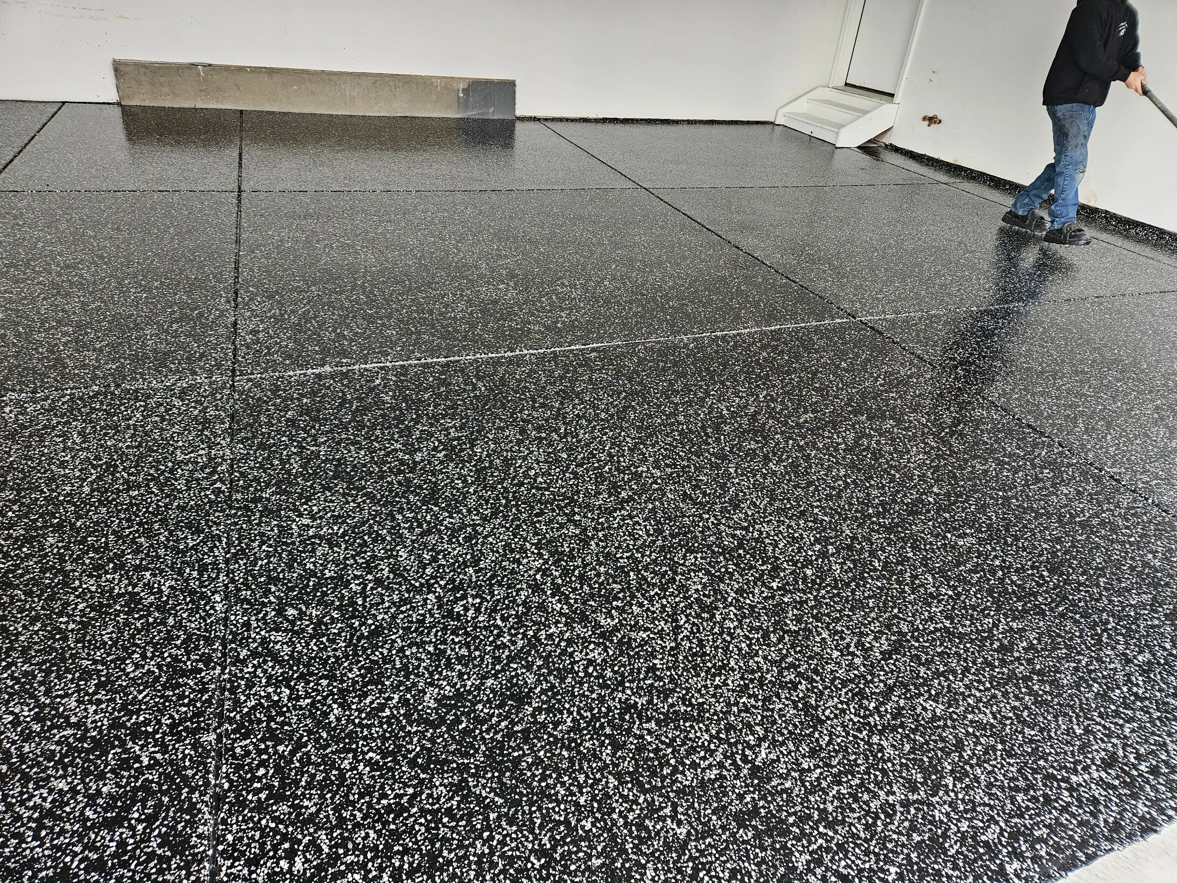 Freshly coated garage floor with a high-gloss epoxy finish and decorative color flake in a Colorado Springs residential garage. The sealed concrete surface reflects overhead lighting and shows no cracks, stains, or tire marks.