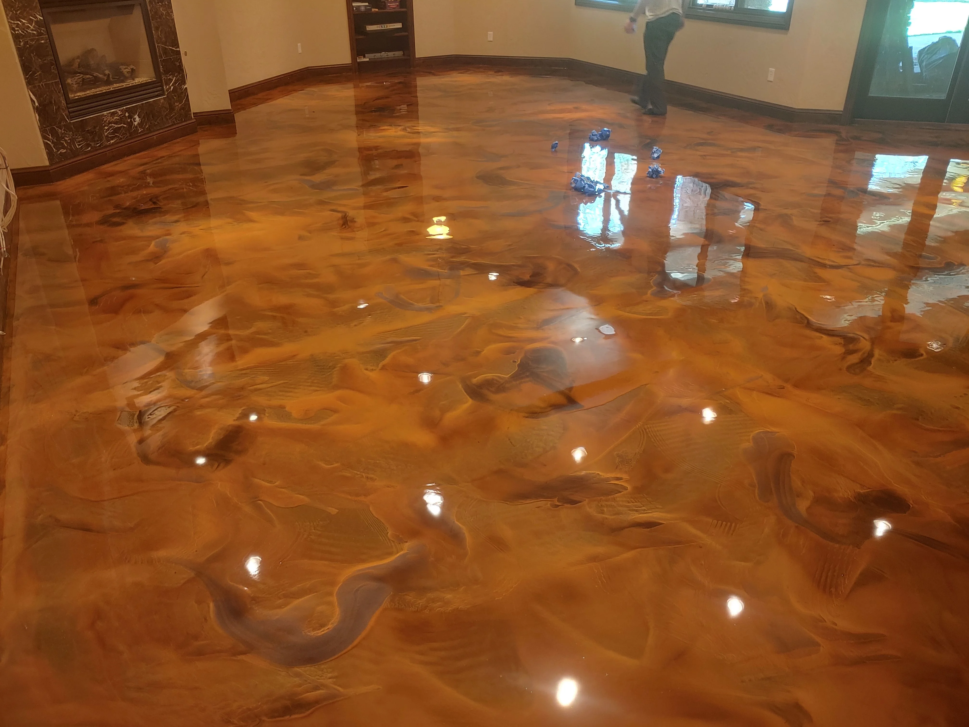 A high-gloss metallic epoxy floor coating with flowing silver and charcoal swirl patterns installed in a residential garage in Colorado Springs, Colorado. The seamless surface reflects overhead lighting and covers the full concrete slab from wall to wall.